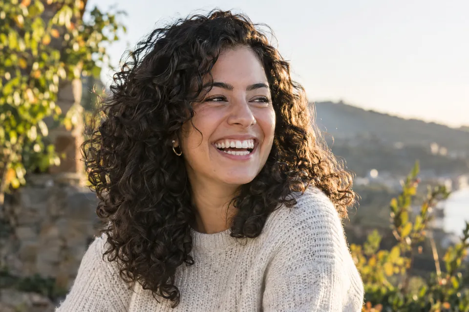 A woman with glossy curly hair laughing in sunlight