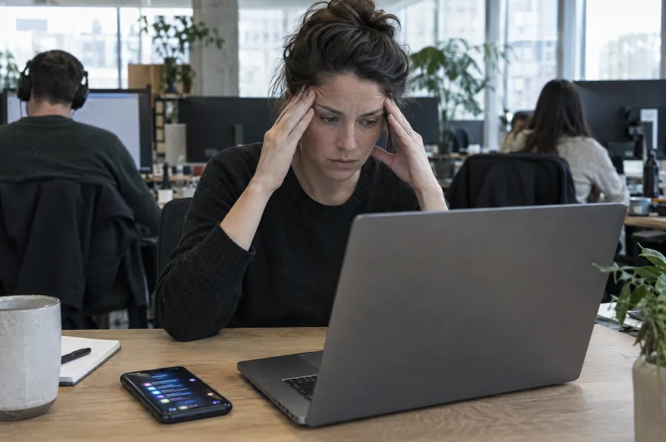 A woman at a laptop pressing her temples
