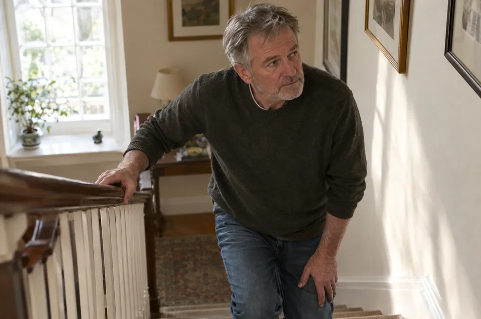 A man in his sixties holding his knee on a staircase