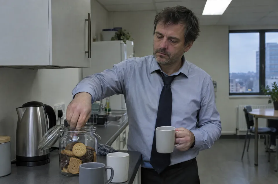 A man reaching into a biscuit jar in an office kitchen