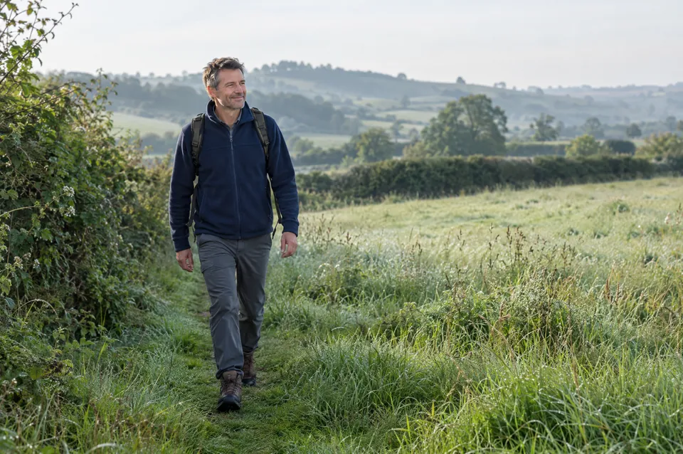 A man walking a footpath through a meadow in early morning light