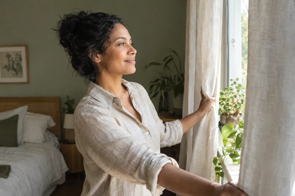 A woman opening the curtains in morning sunlight