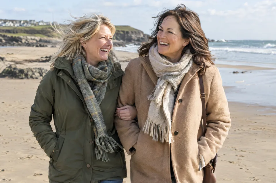 Two women in their fifties walking along a beach, laughing